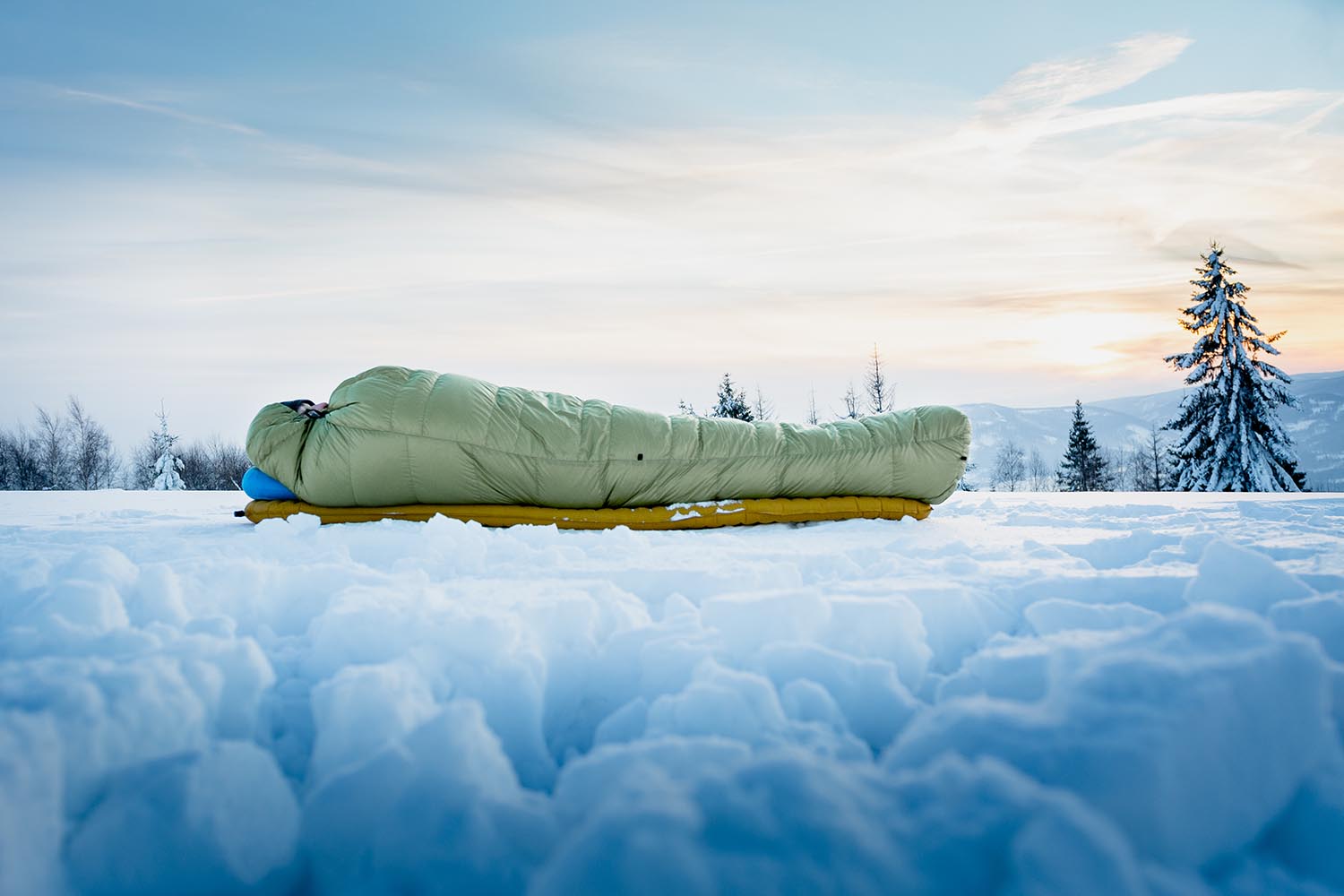 Osoba ležící ve spacáku Cumulus Lite Line 400 v zelené barvě při kempování na sněhu na nafukovací karimatce a polštářku.