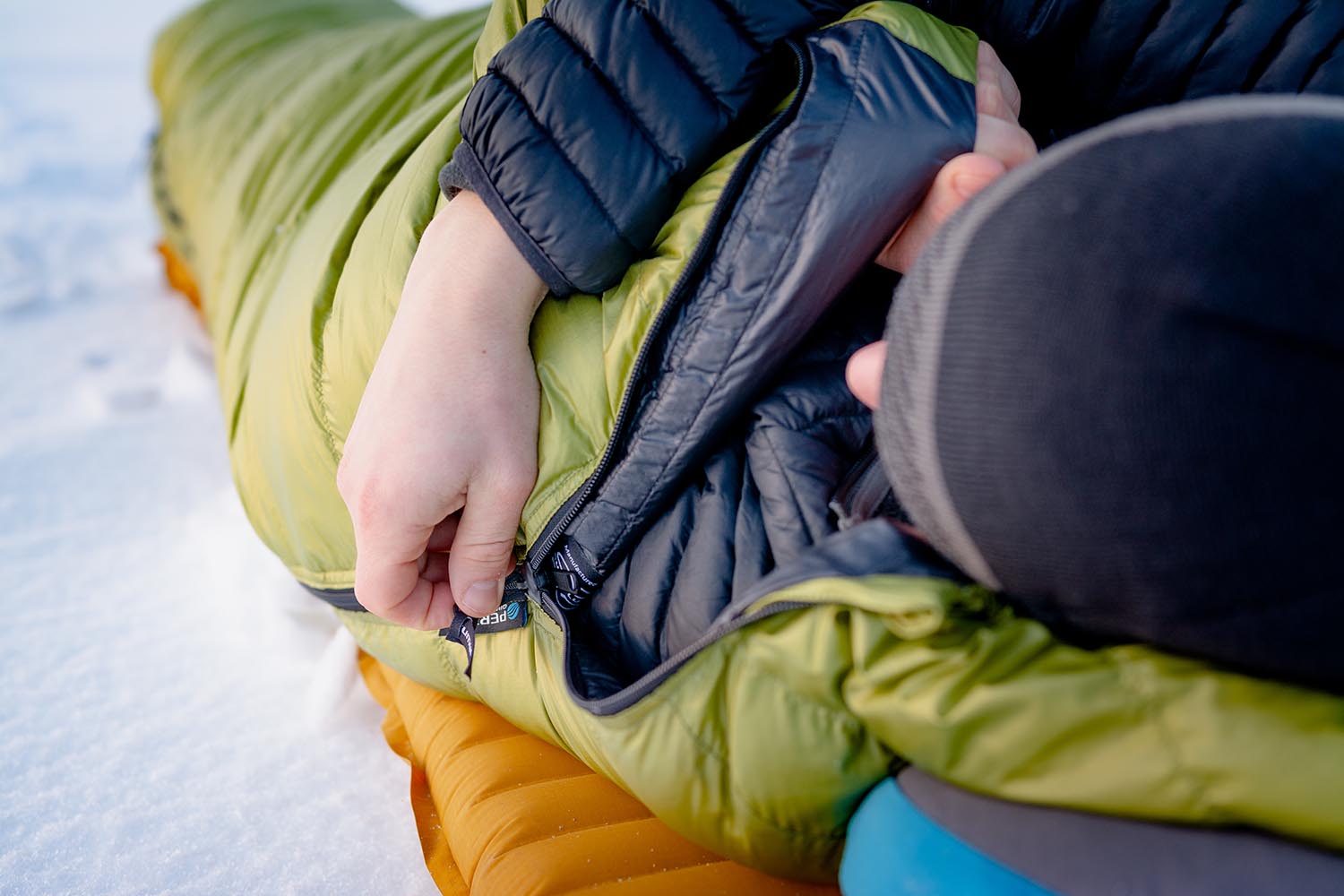 Osoba ležící ve spacáku Cumulus Lite Line 400 v zelené barvě při kempování na sněhu na nafukovací karimatce.