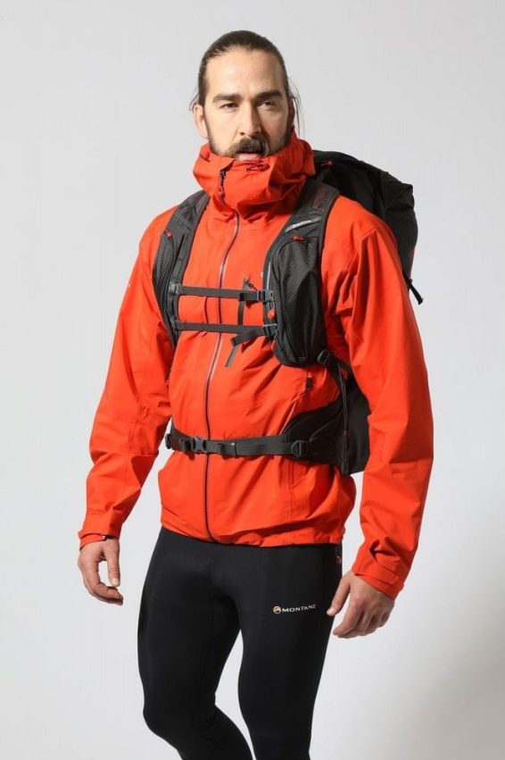 Naplněný batoh Trailblazer 44 v černé barvě na zádech muže. Přední pohled a detail na kapsy na ramenních popruzích.