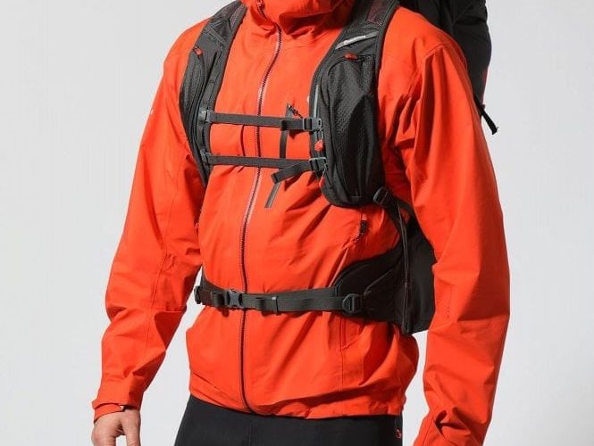 Naplněný batoh Trailblazer 44 v černé barvě na zádech muže. Přední pohled a detail na kapsy na ramenních popruzích.