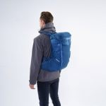 Osoba s batohem Montane Traiblazer 30 na zádech ze zadního bočního pohledu v modré barvě