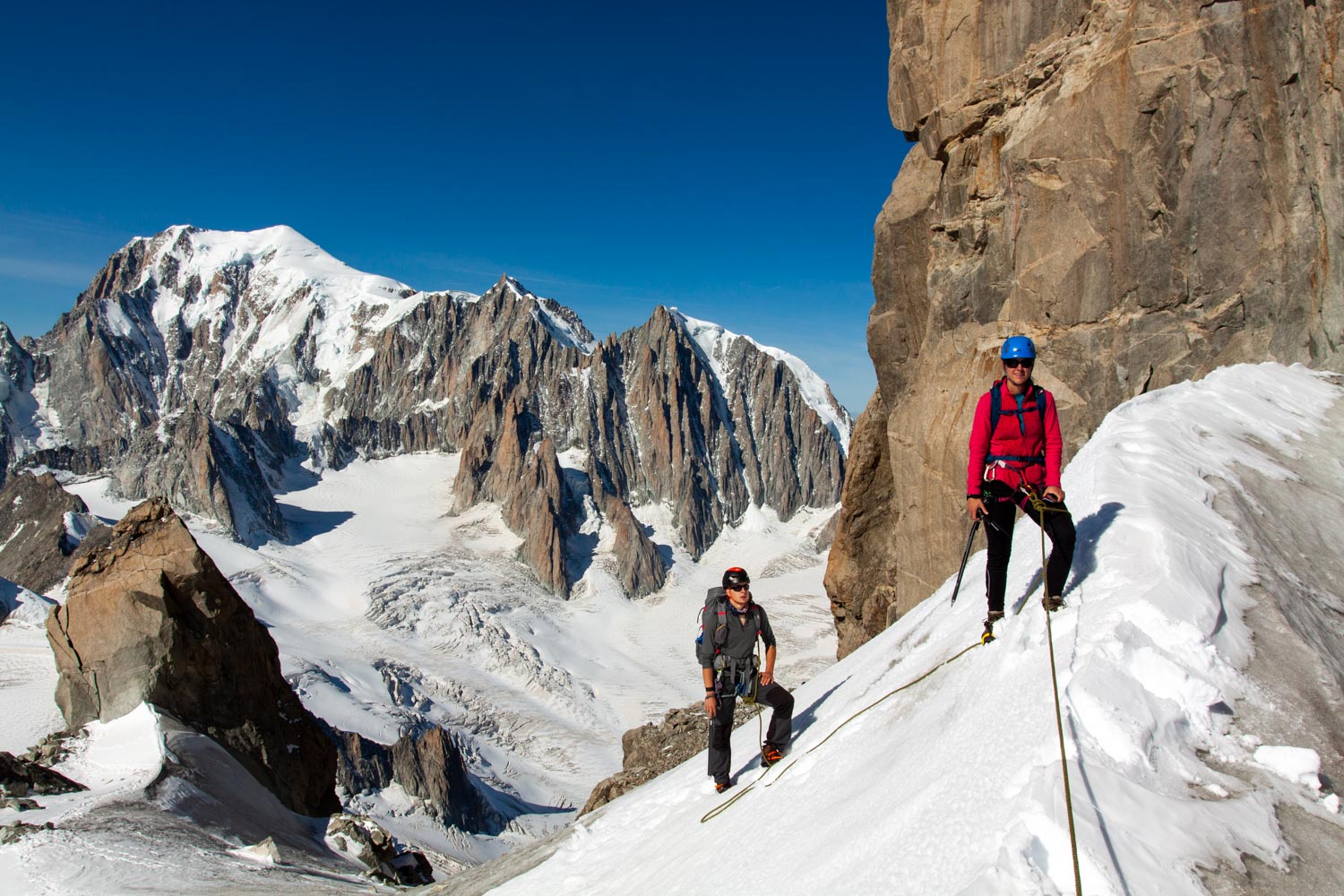 Dva horolezci s výbavou lezoucí na vrchol za krásného počasí v zimě.