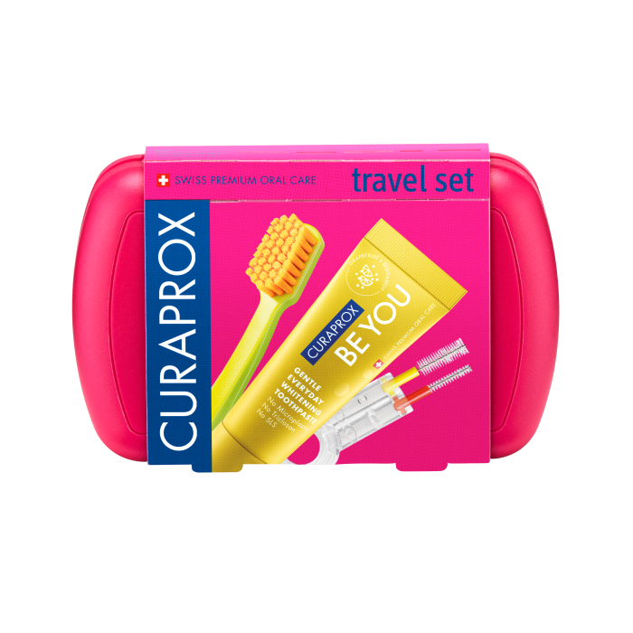 Bright pink travel case containing a Curaprox dental care kit with a yellow toothpaste tube labeled BE YOU and a green toothbrush.