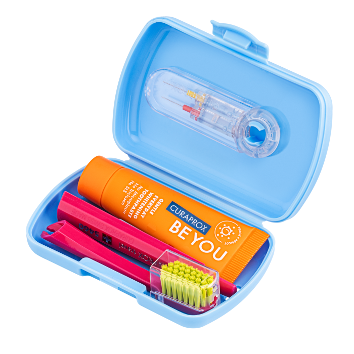 Curaprox Travel Set Modrá 3 Open blue travel dental kit with an orange BE YOU toothpaste tube, a pink handle toothbrush, a small green-bristled brush, and a clear plastic accessory case.