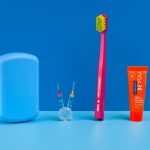 Curaprox Travel Set Modrá 4 Blue travel dental kit with a curved case, pink toothbrush, orange Be You toothpaste, and interdental brushes on a blue surface.