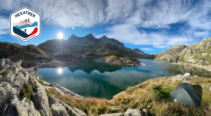 Alpine lake with rocky shores and a camping tent on the right, logo Hexatrek in the upper left.