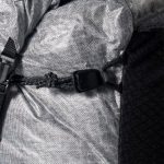 Close-up of a backpack strap with a black plastic buckle on gray fabric.