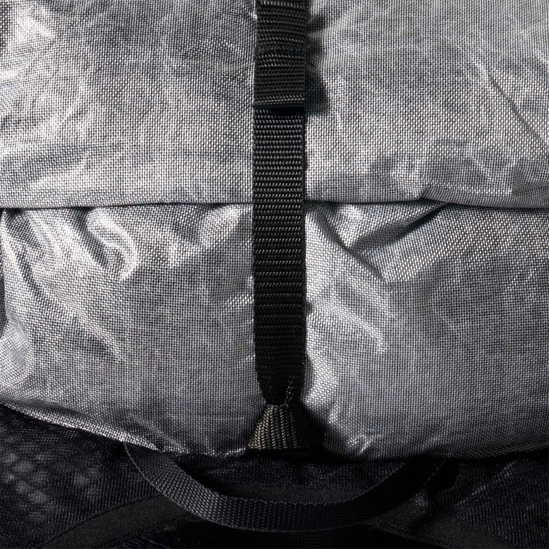Close-up of a gray backpack with a vertical black strap and buckle on textured fabric.