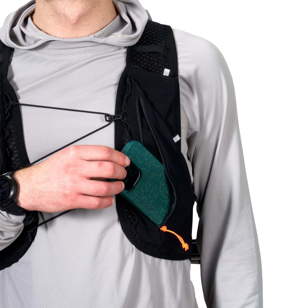 Person wearing a black running vest places a green speckled smartphone into a front pocket while wearing a gray long-sleeve top and a watch.