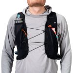 Person wearing a black hydration vest with front bungee cords and a small water bottle in the left pocket, gray long-sleeve shirt underneath.