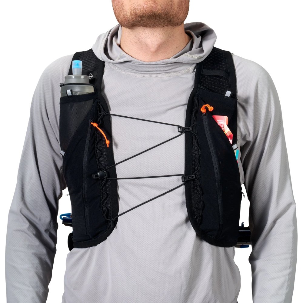 Person wearing a black hydration vest with front bungee cords and a small water bottle in the left pocket, gray long-sleeve shirt underneath.