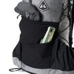 Backpack with a front pocket holding a green multitool and a rolled gray jacket in the side pocket.