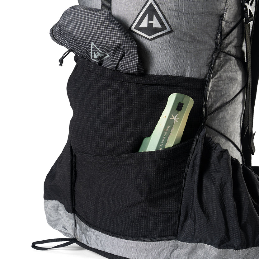 Backpack with a front pocket holding a green multitool and a rolled gray jacket in the side pocket.