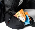 Black waist bag with orange and blue snack packets protruding from its zip pocket ahead of a backpack strap.