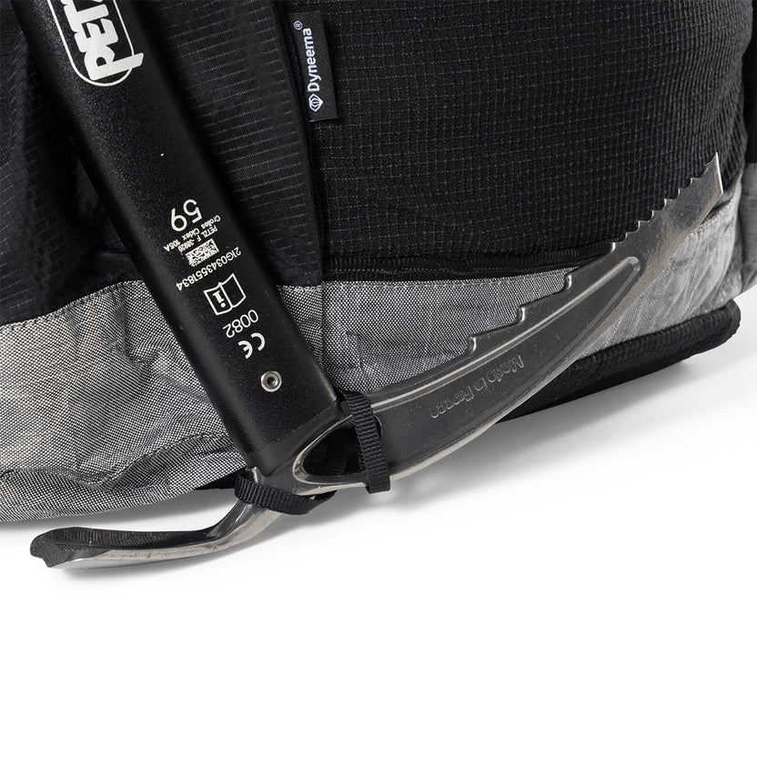 Close-up of a black backpack with an ice axe strapped to its side, featuring a curved pick and metal shaft.