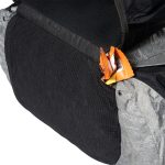 Close-up of a dark backpack with orange candy wrappers sticking out of a pocket pocketed area.