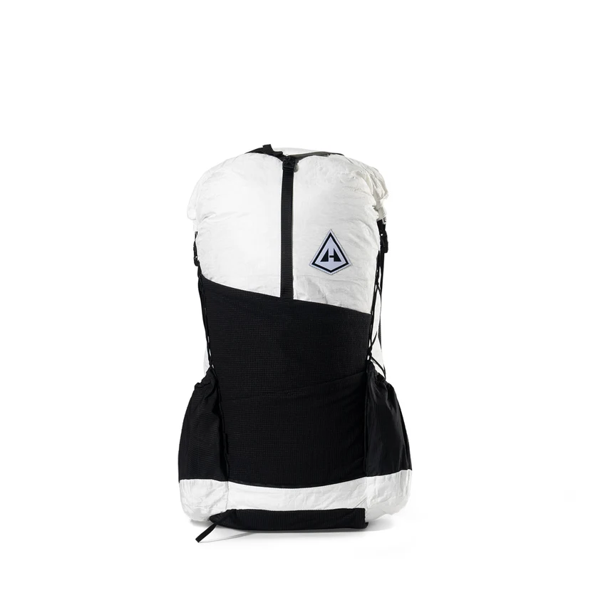 Color-block backpack with white top and black lower section, featuring a front pocket and a triangular logo badge on the upper panel.