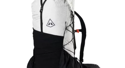 White and black alpine backpack with a large main compartment, front bungee cords, and a padded hip belt; features a side pocket and compact pack design.
