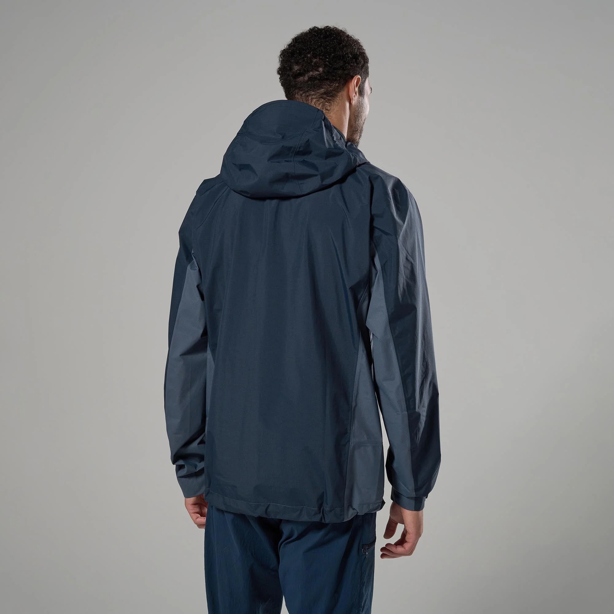 Montane Mens Norste Lite Jacket Eclipse Blue 03 Rear view of a person wearing a navy blue windbreaker against a gray studio backdrop, hood down.