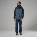 Montane Mens Norste Lite Jacket Eclipse Blue 04 Man wearing a two-tone navy Montane rain jacket and matching pants, standing against a gray background, looking to the left.