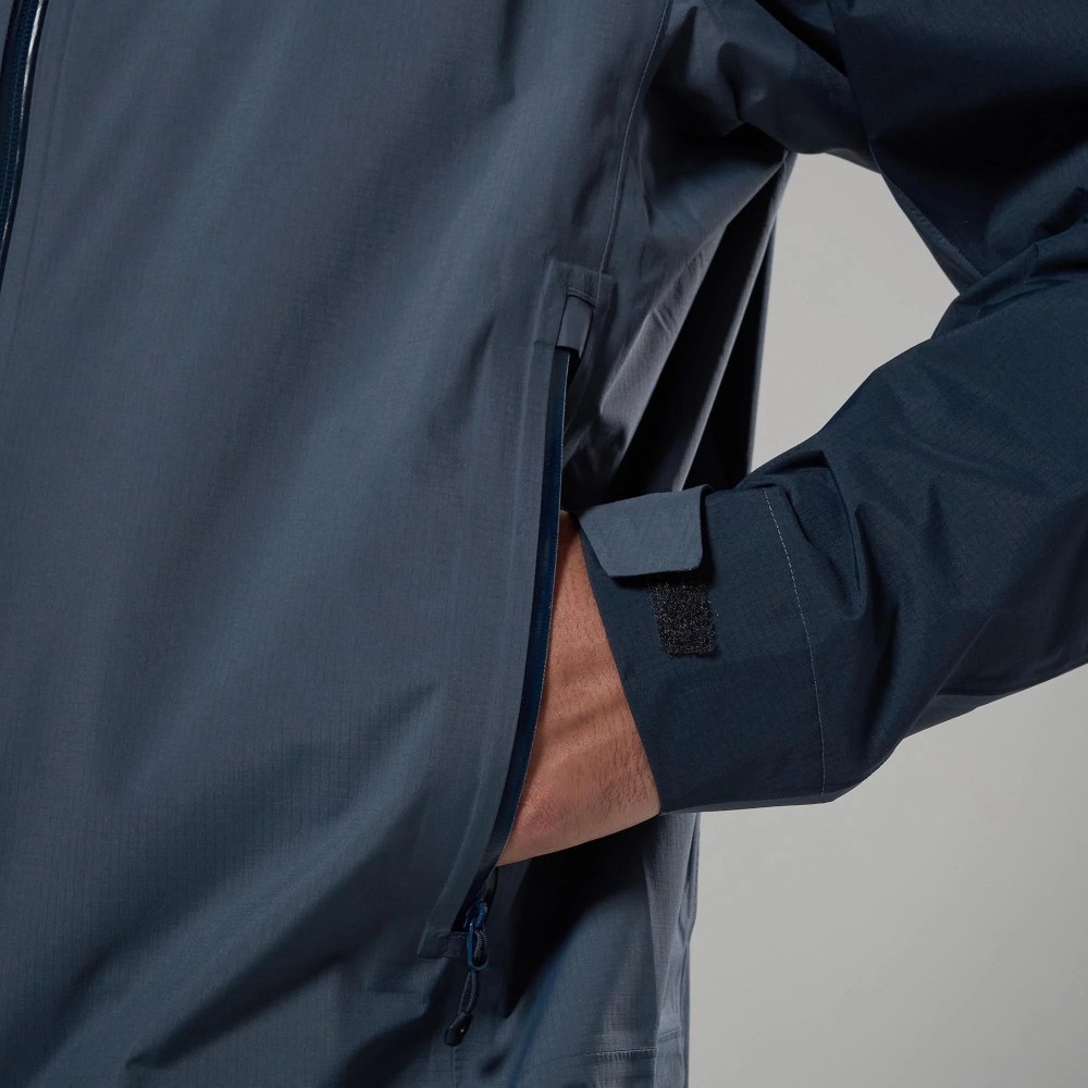 Close-up of a navy outdoor jacket with a zippered side pocket and a hand resting in the pocket.