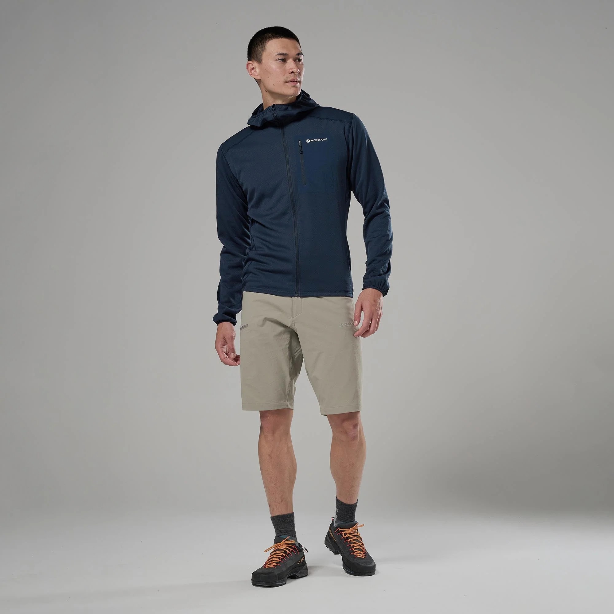 Montane Mens Zepter Hooded Fleece Jacket Eclipse Blue 04 Male model wearing a navy Montane jacket and beige shorts, posing against a gray studio backdrop.