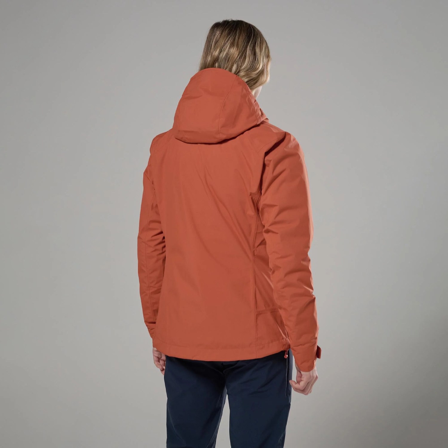 Montane Womens Norste Lite Jacket Lava 02 Back view of a person wearing an orange hooded jacket, standing against a gray background.