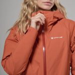 Montane Womens Norste Lite Jacket Lava 04 Close-up of an orange Montane windbreaker with a high collar and central zipper being adjusted by a hand.
