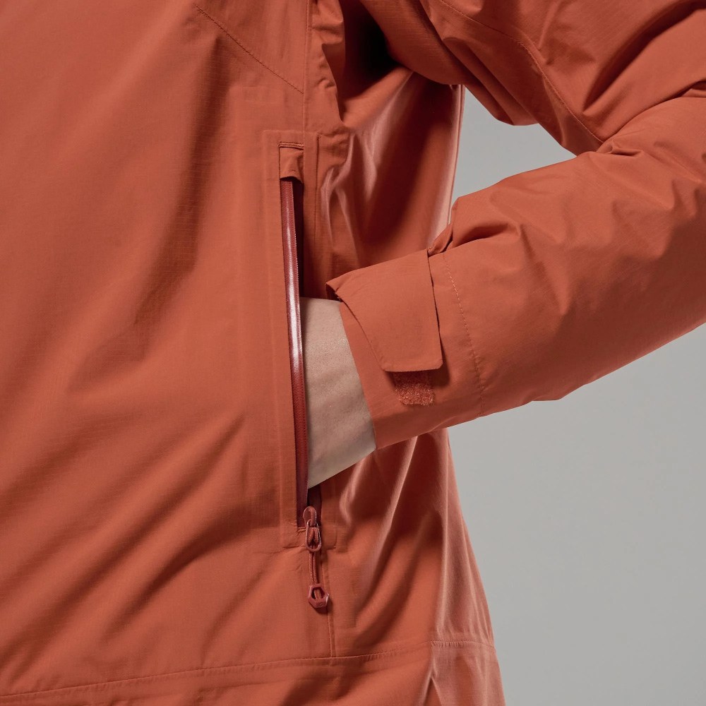 Close-up of an orange rain jacket with a zippered side pocket and a hand slipping into it.