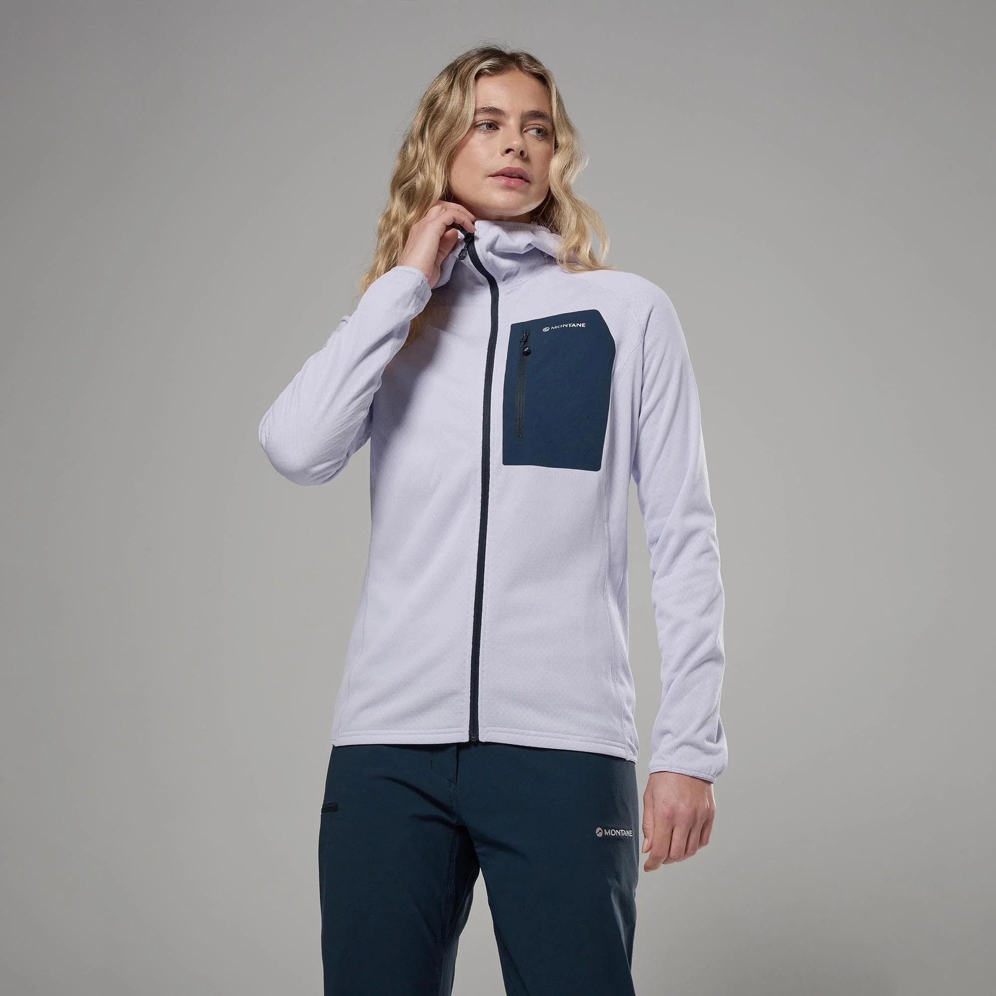 Montane Womens Zepher Hoodie Platinum 02 Woman posing in a light gray Montane jacket with a dark navy chest pocket, looking to the right.