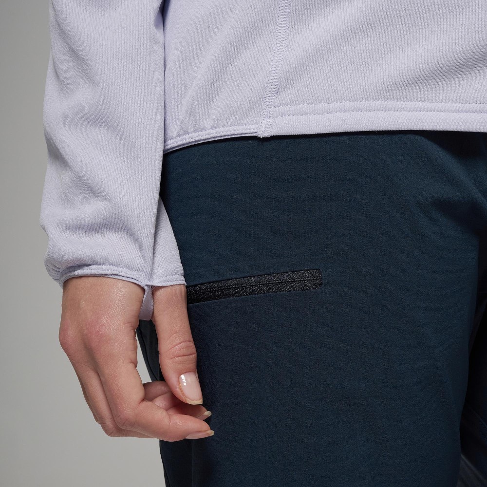 Montane Womens Zepher Hoodie Platinum 06 Close-up of a person's hip area: light purple top over dark blue pants with a small horizontal black zip pocket and a visible hand nearby